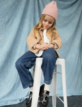 Girl wearing pink knit hat and jeans sitting cross-legged in soft natural light – kids fashion editorial photography by Miriam Dang 