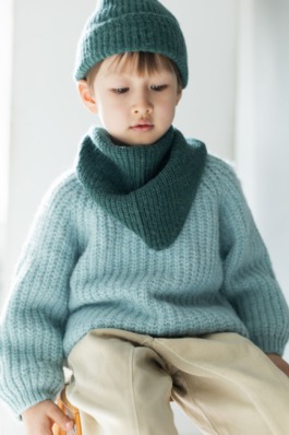 Child in cosy blue knitwear sitting on wooden boxes in a minimal studio — Scandinavian kids fashion editorial. 