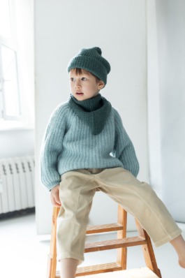 Child in cosy blue knitwear sitting on wooden boxes in a minimal studio — Scandinavian kids fashion editorial. 