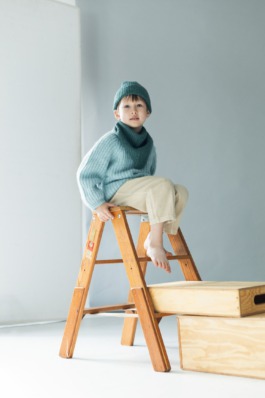 Child in cosy blue knitwear sitting on wooden boxes in a minimal studio — Scandinavian kids fashion editorial. 