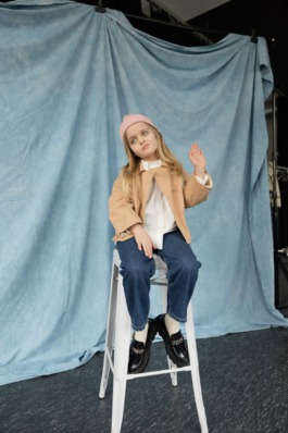 Girl wearing pink knit hat and jeans sitting cross-legged in soft natural light – kids fashion editorial photography by Miriam Dang