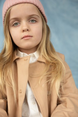 Girl wearing pink knit hat and jeans sitting cross-legged in soft natural light – kids fashion editorial photography by Miriam Dang