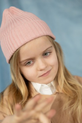 Girl wearing pink knit hat and jeans sitting cross-legged in soft natural light – kids fashion editorial photography by Miriam Dang